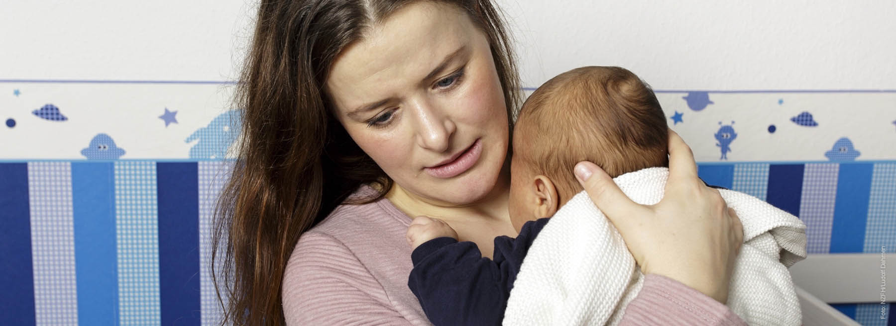 Gestresste Mutter hält schreiendes Baby im Arm an sich gedrückt