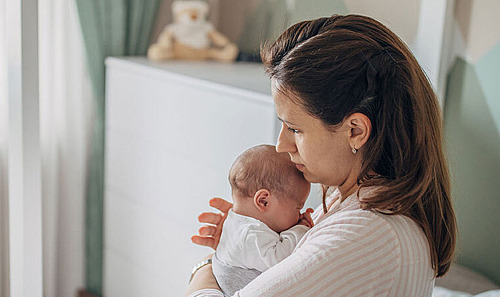 Eine Mutter hält ihr Baby im Schlafzimmer auf dem Bett im Arm.
