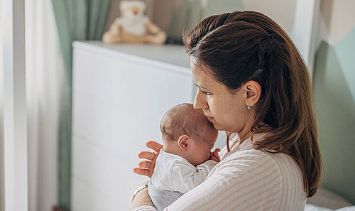 Eine Mutter hält ihr Baby im Schlafzimmer auf dem Bett im Arm.