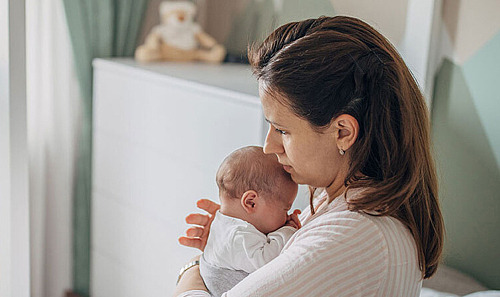 Eine Mutter hält ihr Baby im Schlafzimmer auf dem Bett im Arm.