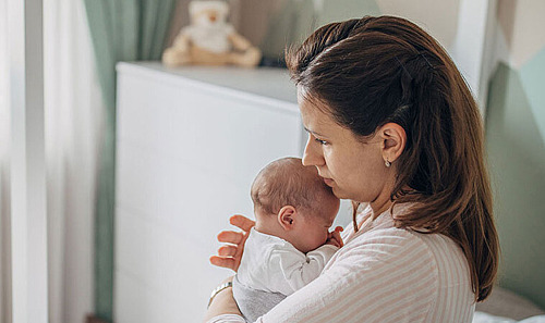 Eine Mutter hält ihr Baby im Schlafzimmer auf dem Bett im Arm.