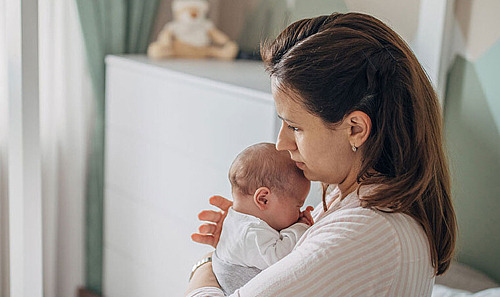 Eine Mutter hält ihr Baby im Schlafzimmer auf dem Bett im Arm.