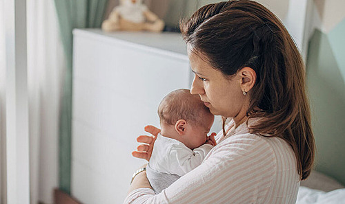 Eine Mutter hält ihr Baby im Schlafzimmer auf dem Bett im Arm.