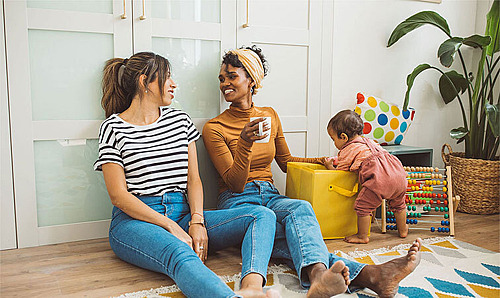 Zwei Frauen sitzen auf dem Boden und spielen mit ihrem Kind.