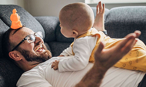 Junger Vater und Baby entspannen gemeinsam auf dem Sofa.
