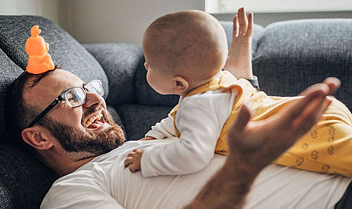 Junger Vater und Baby entspannen gemeinsam auf dem Sofa.