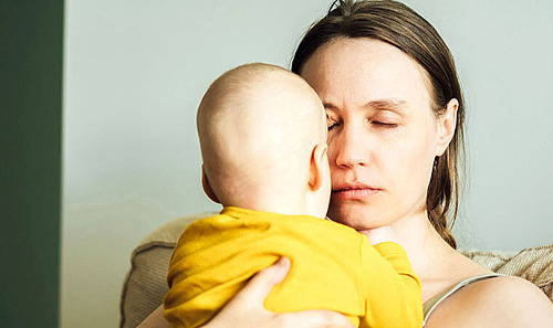 Eine müde Mutter hat die Augen geschlossen und hält ihr Baby im Arm.