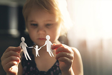 Ein Kind betrachtet die aus Papier ausgeschnittene Silhouette einer Familie.