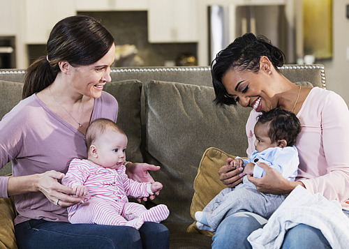 Zwei Mütter sitzen auf einem Sofa mit ihren Babys auf dem Schoß