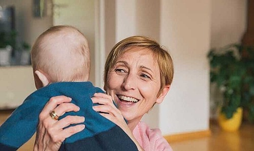 Eine Frau hält lächelnd ein Baby hoch