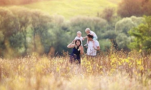 Vater und Mutter laufen mit ihren Kindern auf den Schultern durch ein Feld