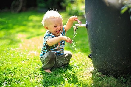 Auch sehr flaches Wasser kann für Babys und Kleinkinder gefährlich sein Ein Kind spielt mit dem Wasserhahn einer Regentonne.