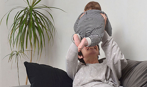 Mutter liegt auf dem Sofa und hebt ihr Baby hoch.