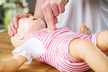An einer Babypuppe werden Erste-Hilfe-Maßnahmen gezeigt.
