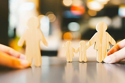 Mutter, Vater und zwei Kinder als kleine Holzfiguren. Die Kinder stehen zwischen den Eltern, der Vater steht etwas entfernt.