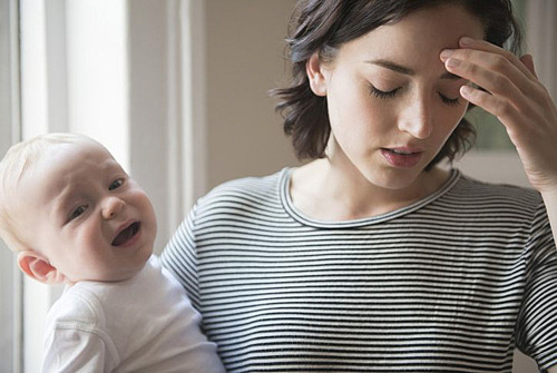 Mutter mit weinendem Baby im Arm greift sich an den Kopf 