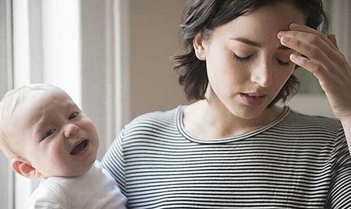 Mutter mit weinendem Baby im Arm greift sich an den Kopf 