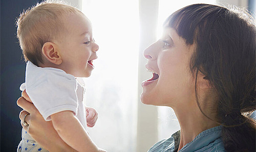 Eine Mutter hält ihr Baby nah ans Gesicht. Die beiden lachen sich an.