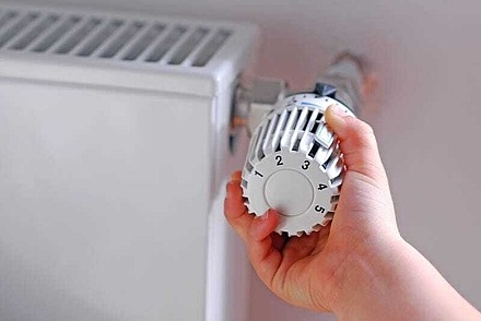 Eine Hand dreht am Thermostat eines Heizkörpers