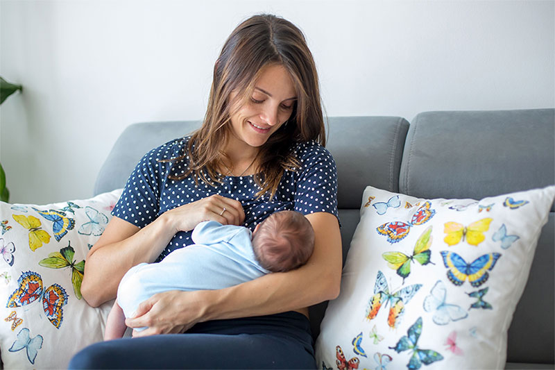 Eine Mutter sitzt auf dem Sofa und stillt ihr Baby.
