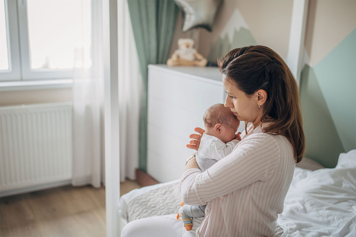 Eine Mutter hält ihr Baby im Schlafzimmer auf dem Bett im Arm.