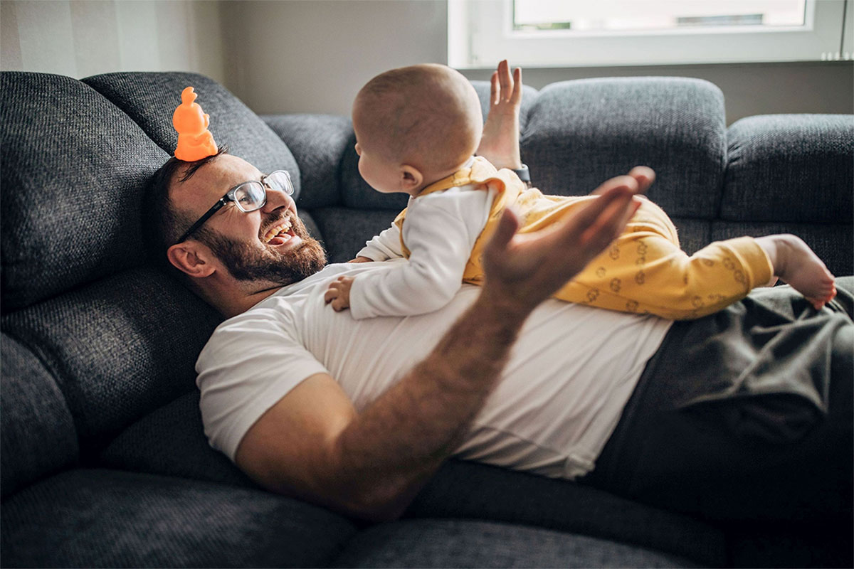 Junger Vater und Baby entspannen gemeinsam auf dem Sofa.