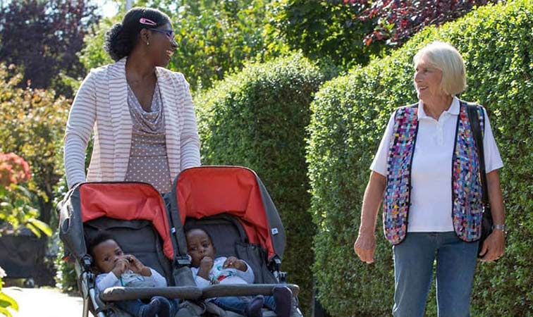 Mutter mit Zwillings-Kinderwagen spricht mit Familienpatin 