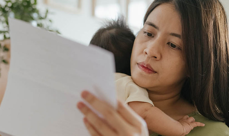 Mutter mit Baby auf dem Arm prüft ein Dokument