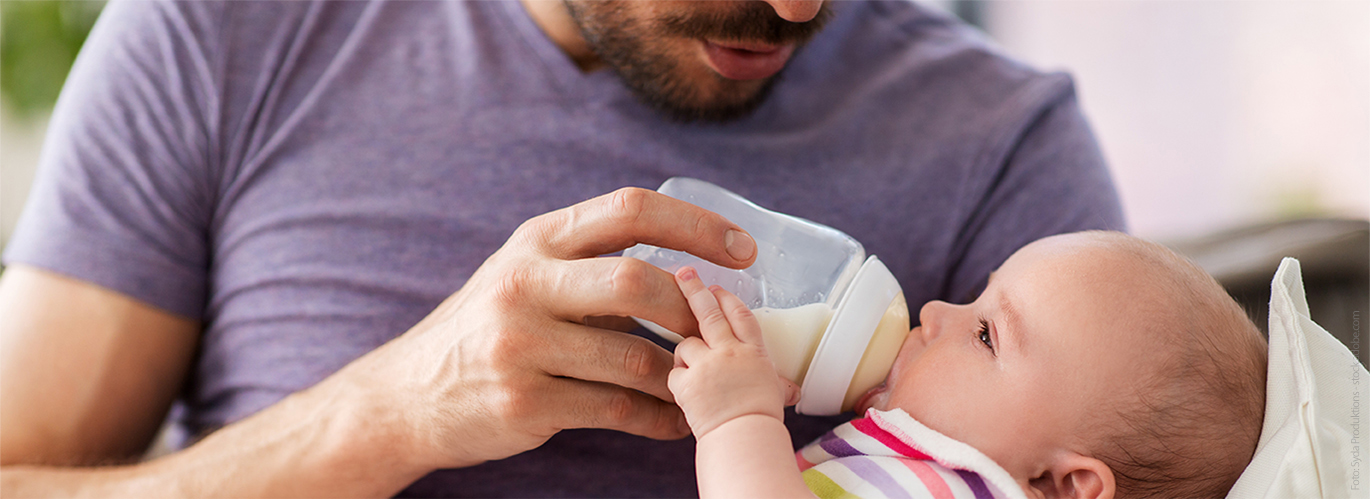 Eine einfühlsame Flaschenfütterung schafft Nähe und Bindung Ein Vater hält sein Baby im Arm und füttert es mit der Flasche