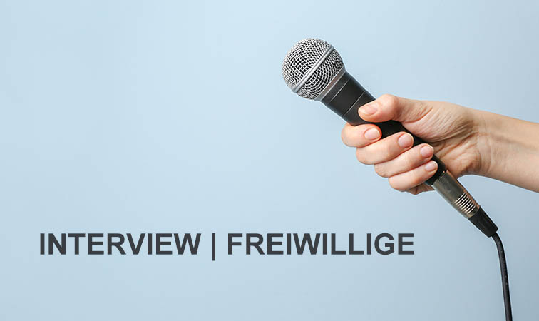 Eine Hand hält ein Mikrofon. Auf dem Hintergrund steht folgender Text: Interview Freiwillige