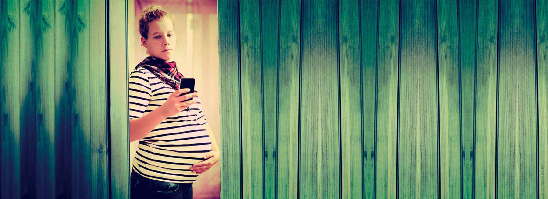 Schwangere Frau mit einem Handy in der Hand